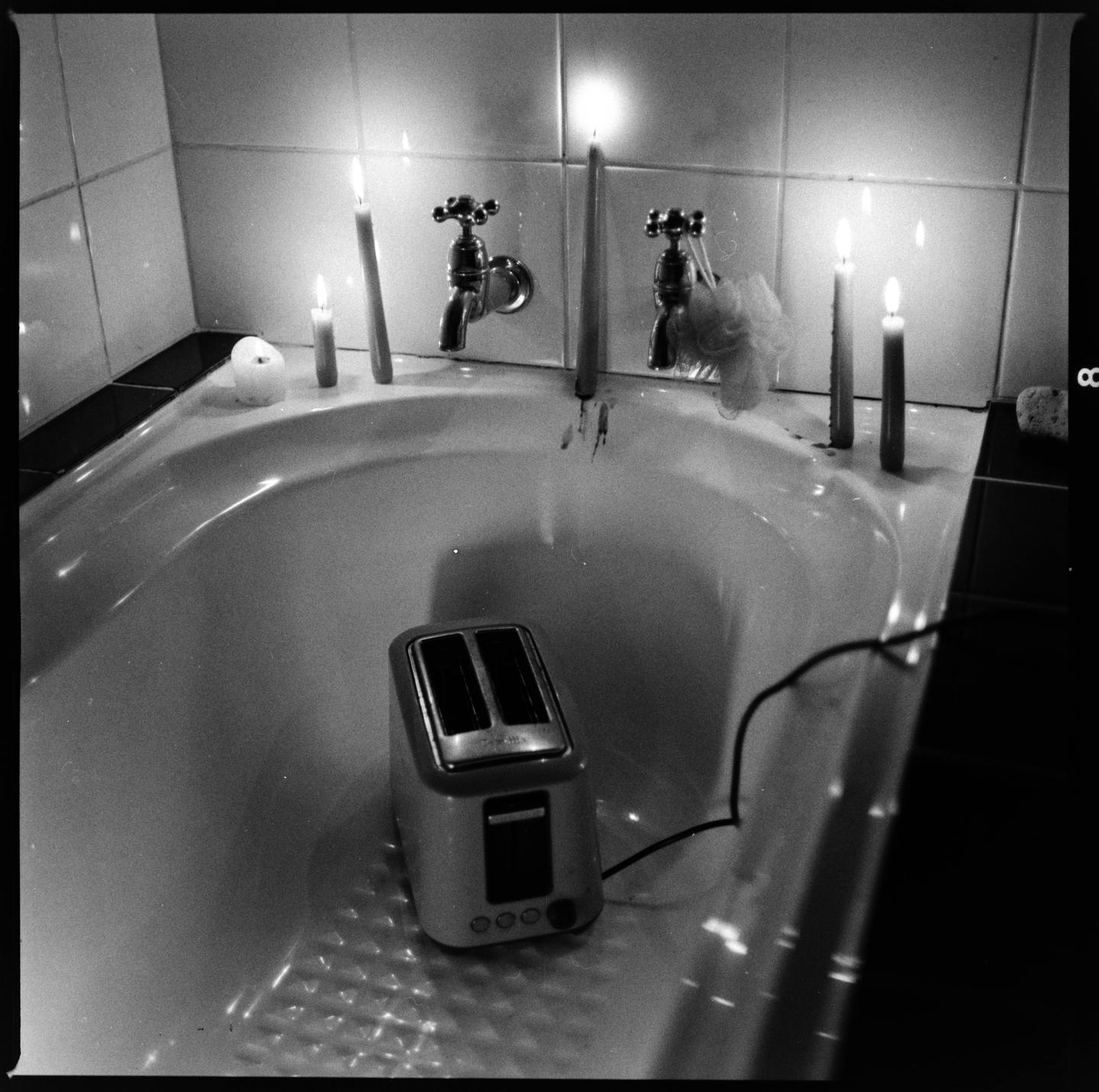 A toaster sits in a bathtub surrounded by lit candles.