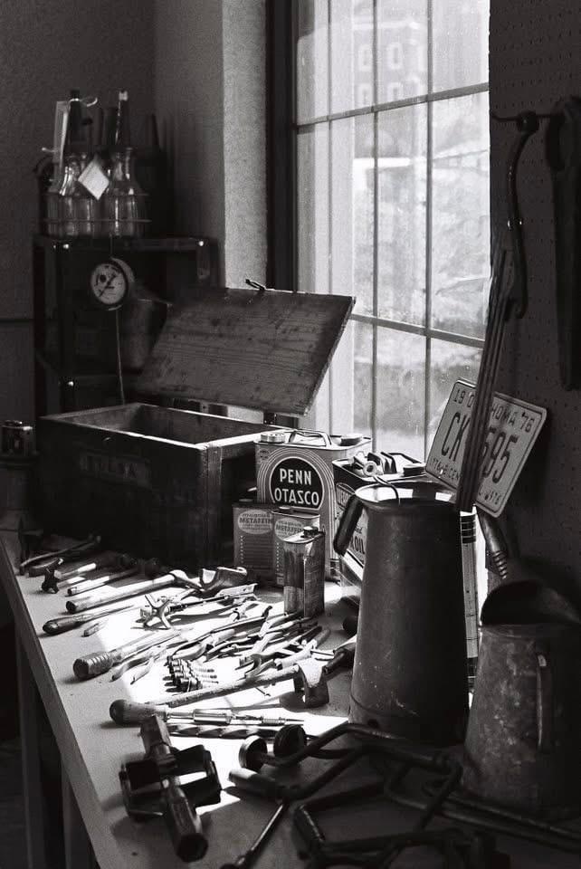 A collection of tools and containers are arranged on a workbench next to a window.