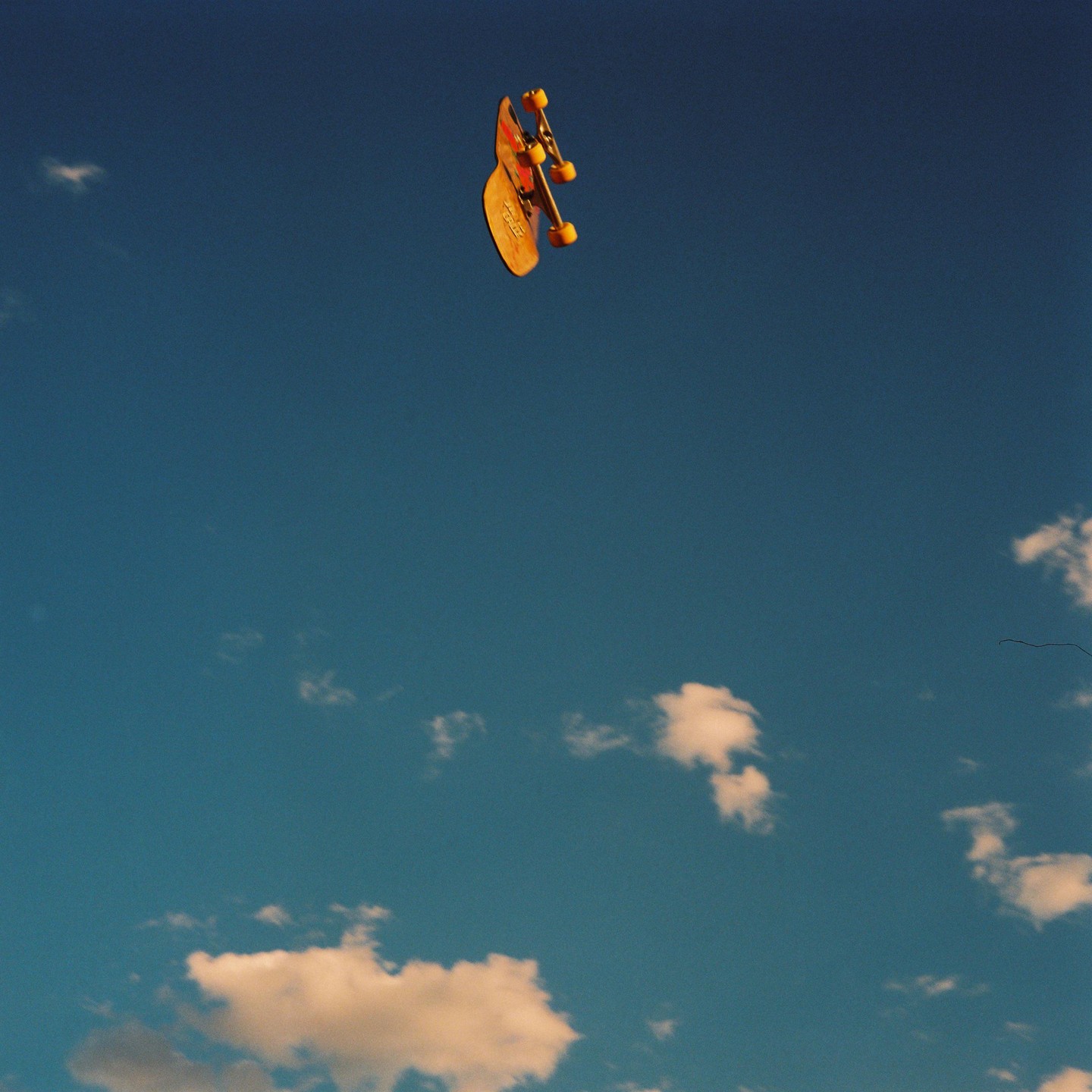 A skateboard is suspended in a clear blue sky with scattered white clouds.