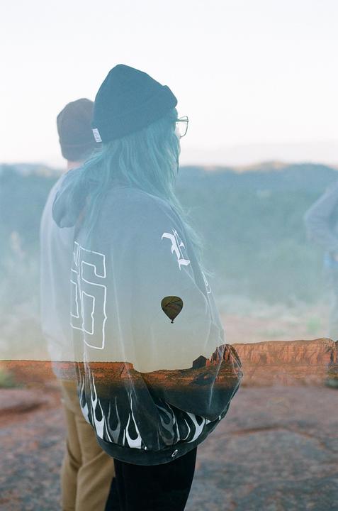 A double exposure shows a woman with blue hair and a man looking out over a desert landscape with a hot air balloon.
