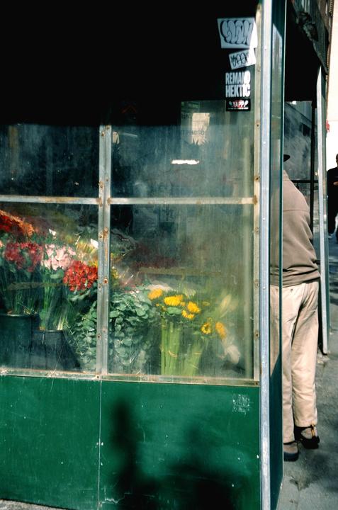 A person stands next to a green flower stall with various bouquets visible through the glass.