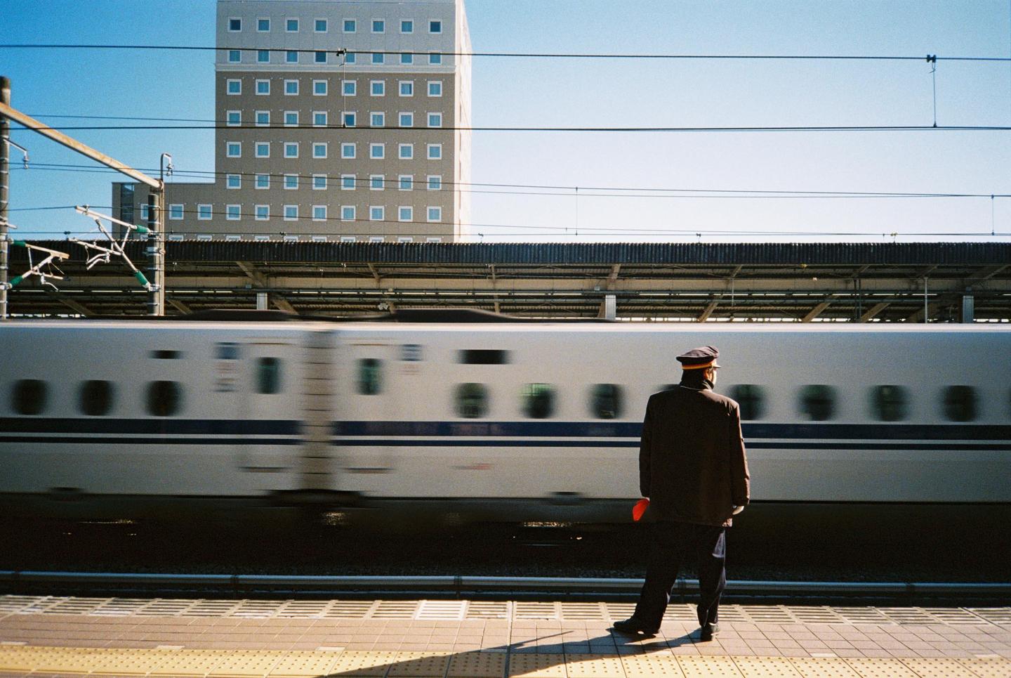 A man in uniform stands on a train platform as a bullet train speeds past.
