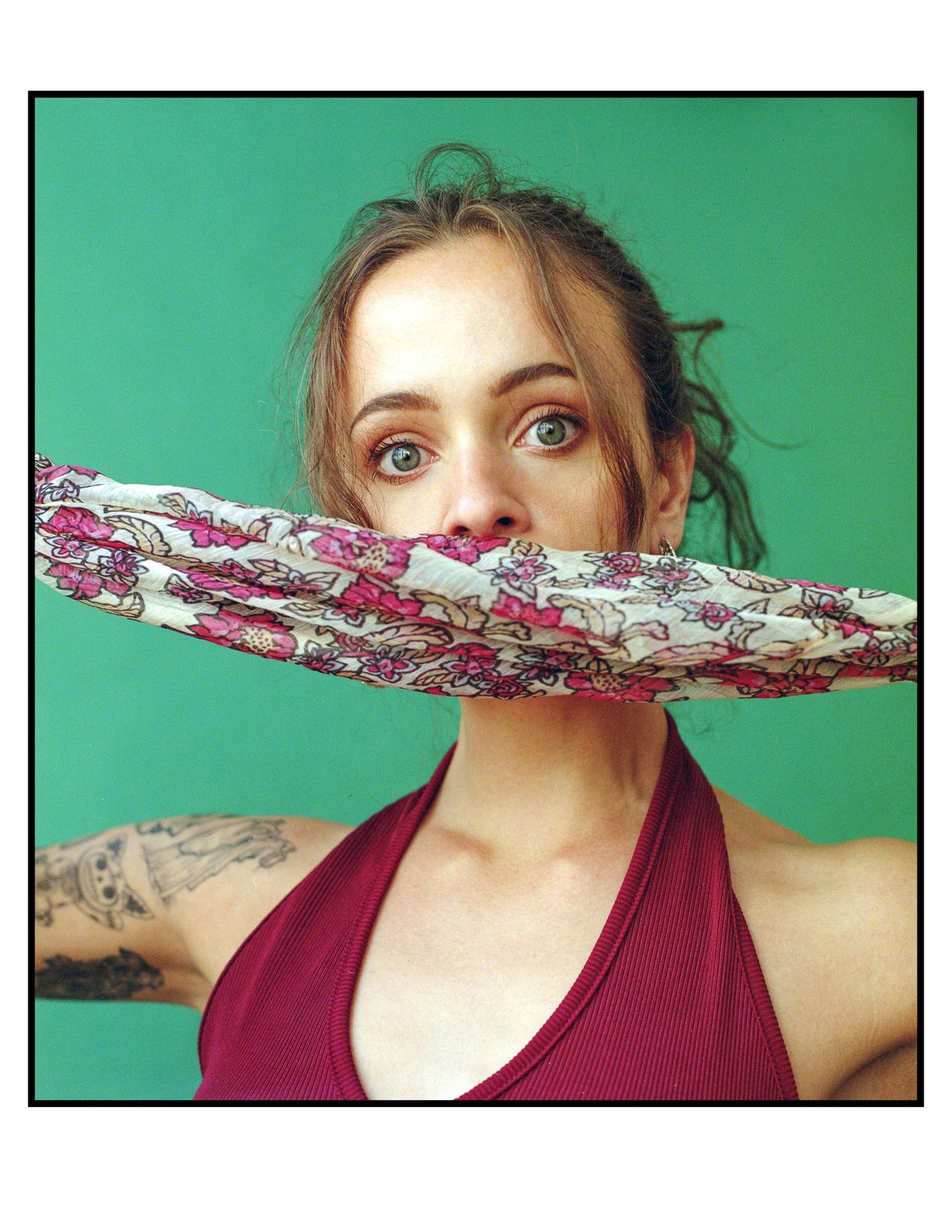 A woman with a floral scarf covering her mouth looks directly at the viewer.
