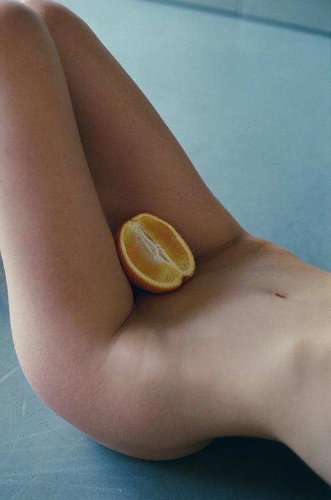 A half orange rests on a woman's thigh and hip.