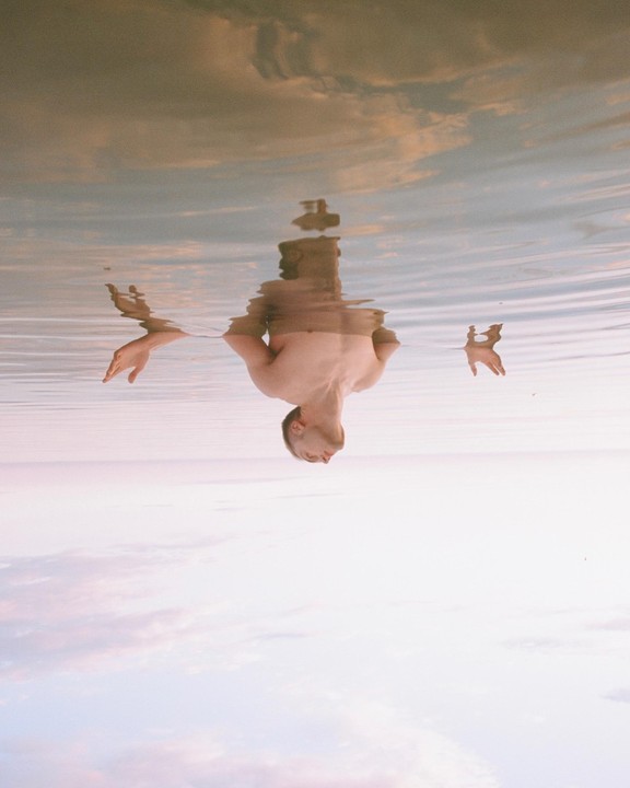 A man is upside down in the water with his head and hands visible above the surface.