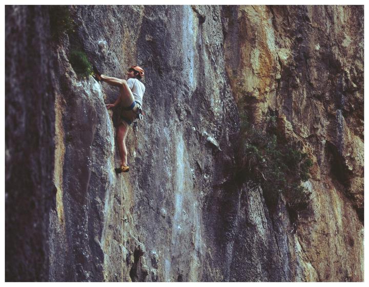 A man in a helmet and harness climbs a rock face.