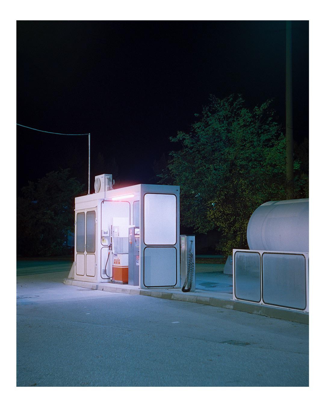 A gas station with a single pump and a large tank is illuminated at night.