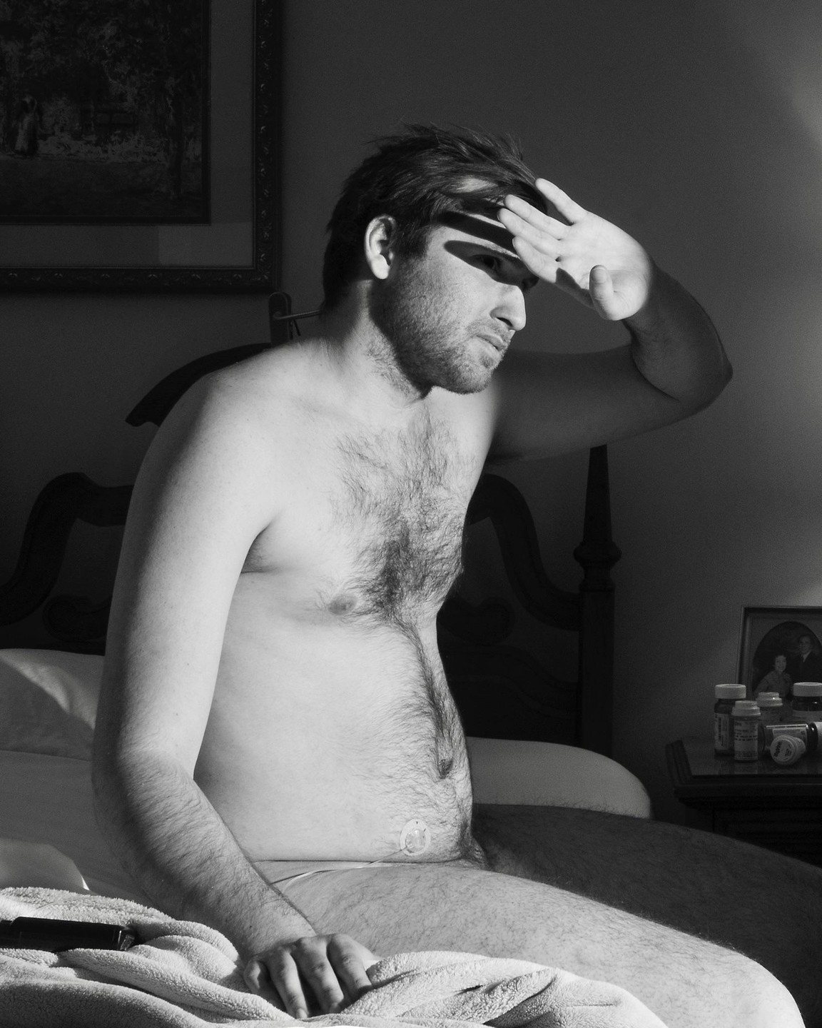 A man sits on a bed, shielding his eyes from the sun.