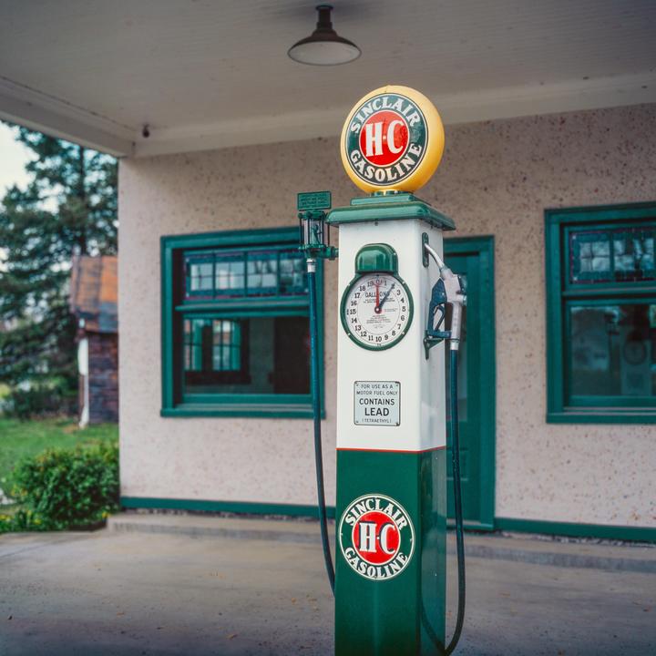 A vintage Sinclair gasoline pump stands in front of a building with green-framed windows.