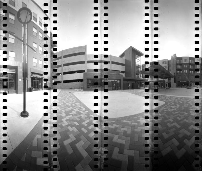 A wide-angle view shows a modern building complex with a parking garage and a patterned brick plaza.