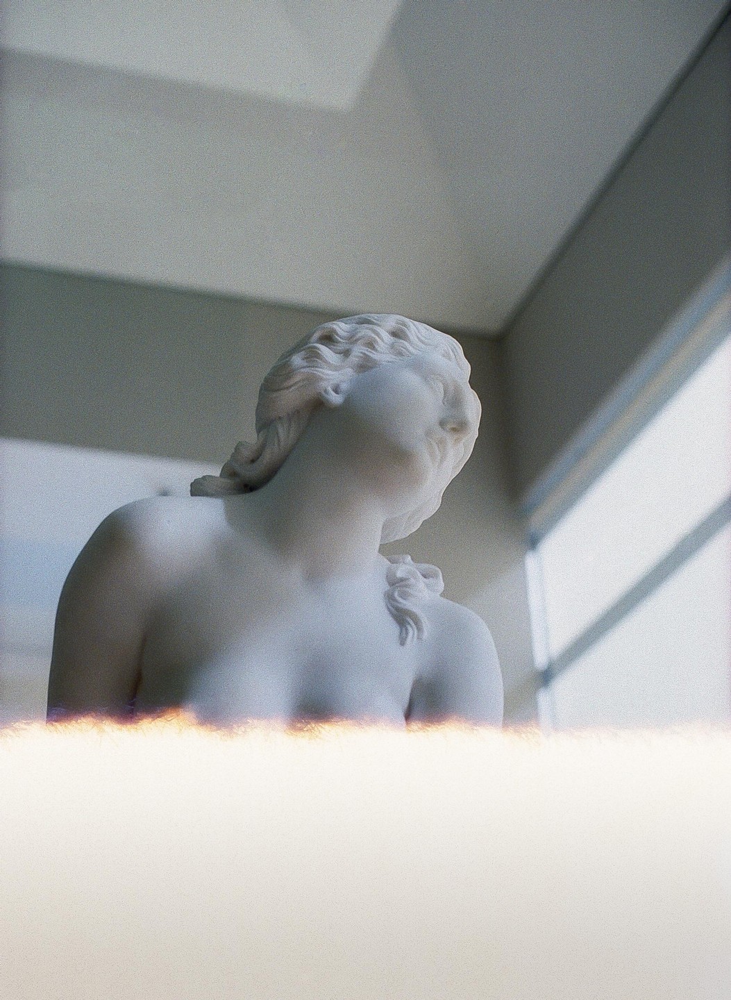 A white marble statue of a woman is shown from the chest up, looking towards a window with light streaming in.
