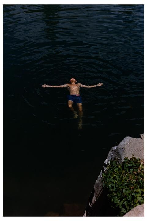 A man floats on his back in dark water with his arms outstretched.