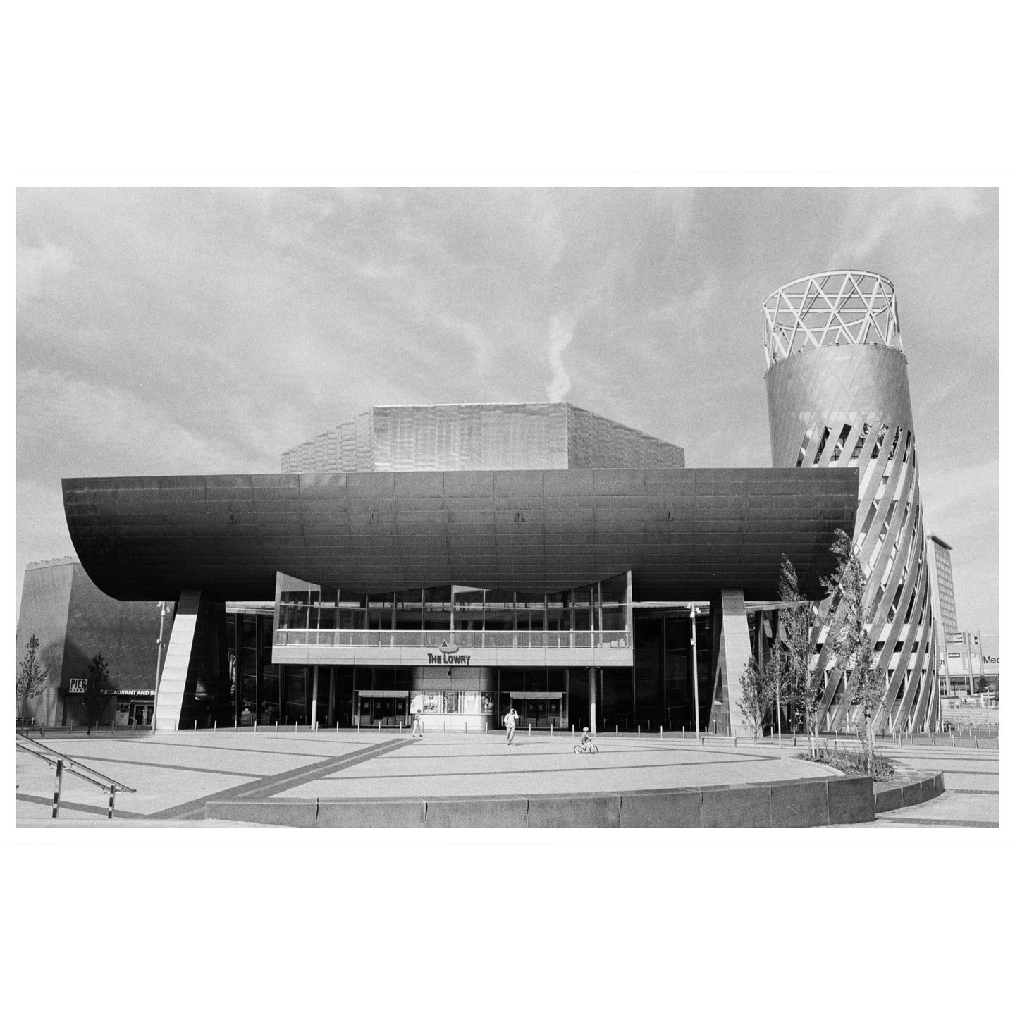 The Lowry Theatre is visible with a tall, twisted building next to it, and a person on a bicycle in the foreground.