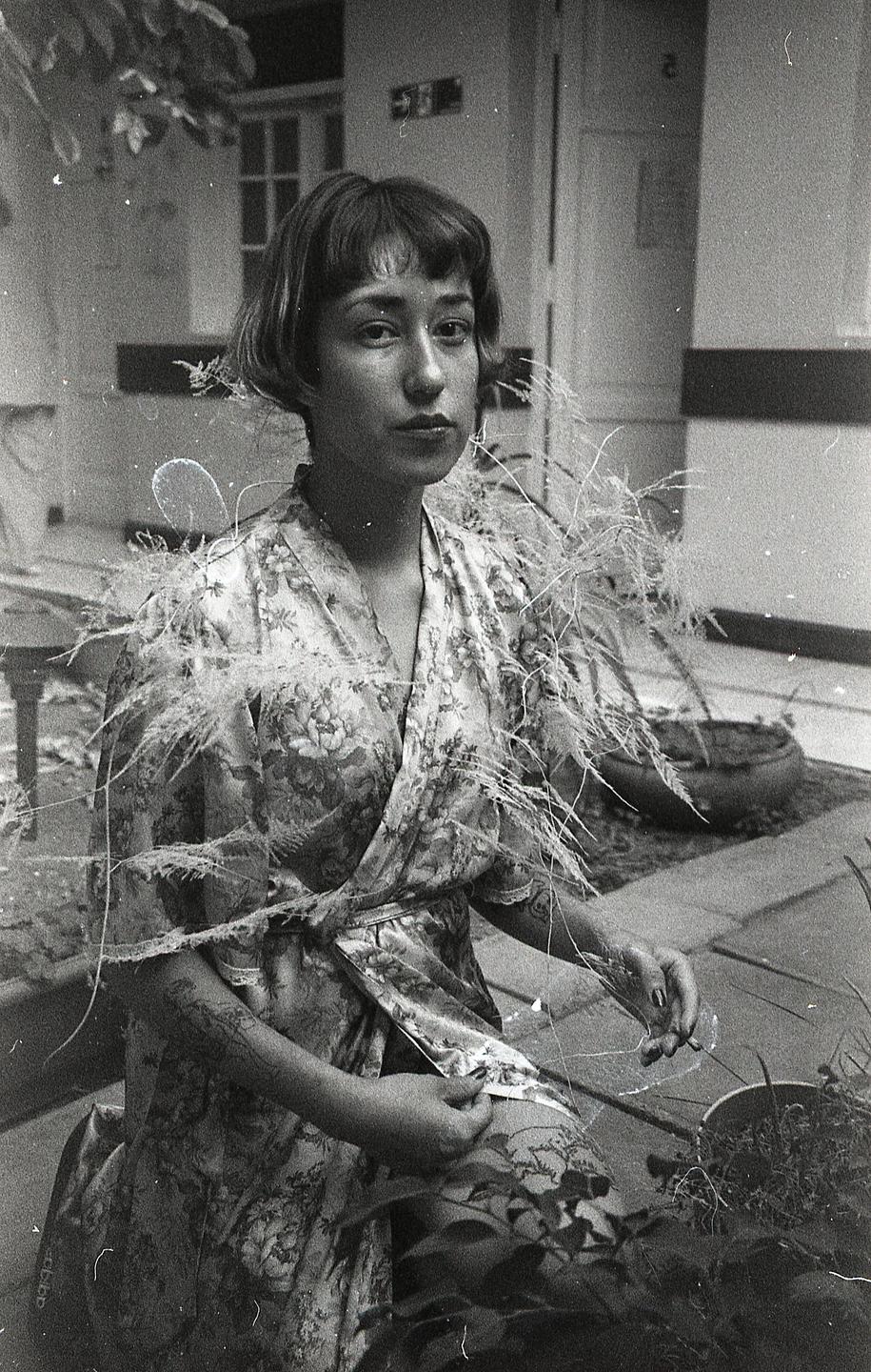 A woman in a floral robe with feathery adornments poses for a self-portrait.