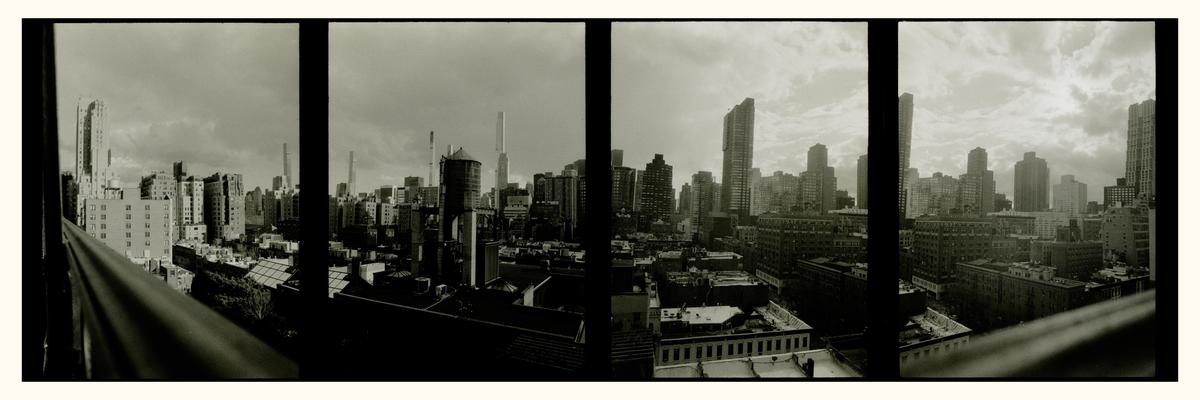 A panoramic view of a city skyline with numerous buildings and a water tower is seen from a terrace.