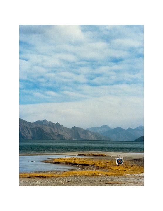 A target stands on a grassy shore next to a body of water with mountains in the distance under a cloudy sky.