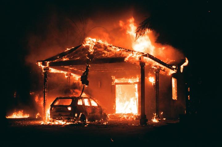 A house and a car are engulfed in flames at night.