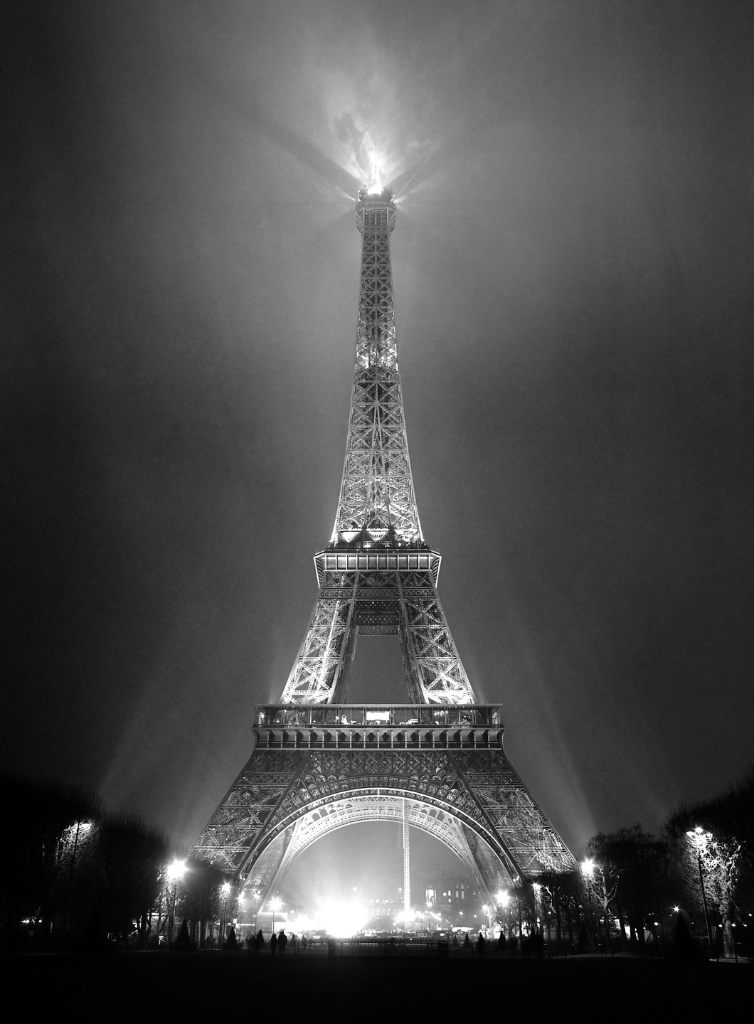 The Eiffel Tower is illuminated at night, with light beams extending into the hazy sky.