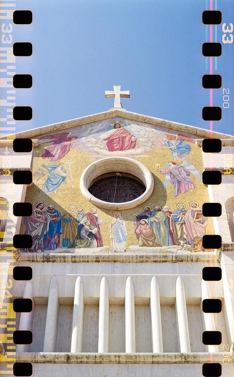 A mosaic depicting religious figures adorns the facade of a church under a clear blue sky.