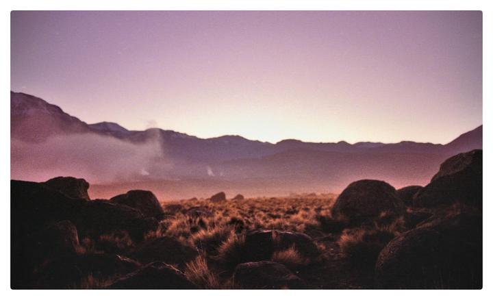 A vast landscape of mountains and plains is illuminated by the first light of dawn.