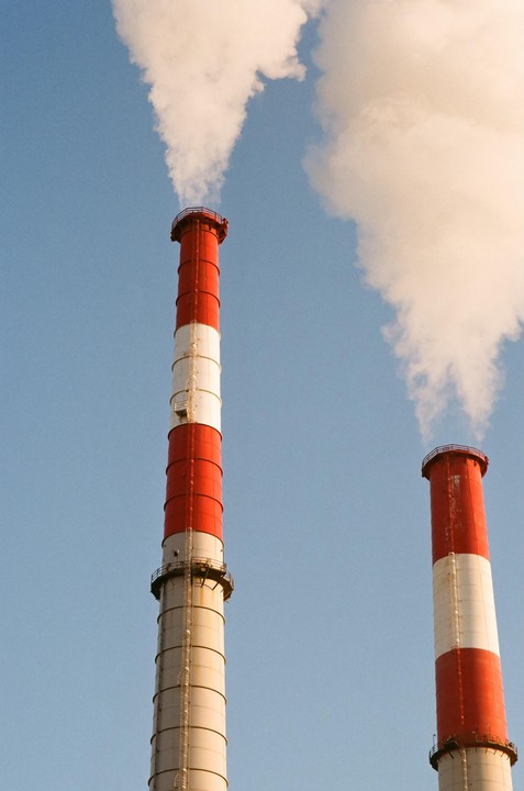 Two red and white striped smokestacks emit white smoke into a clear blue sky.