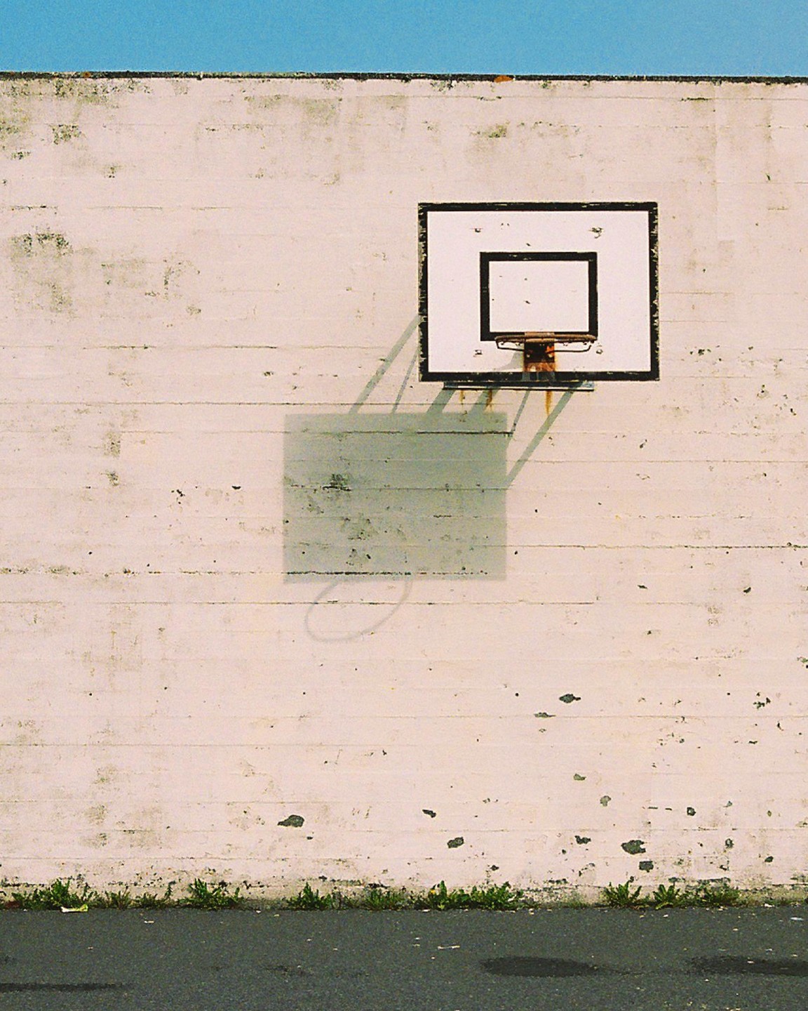 A basketball hoop is mounted on a weathered concrete wall with a clear blue sky above.