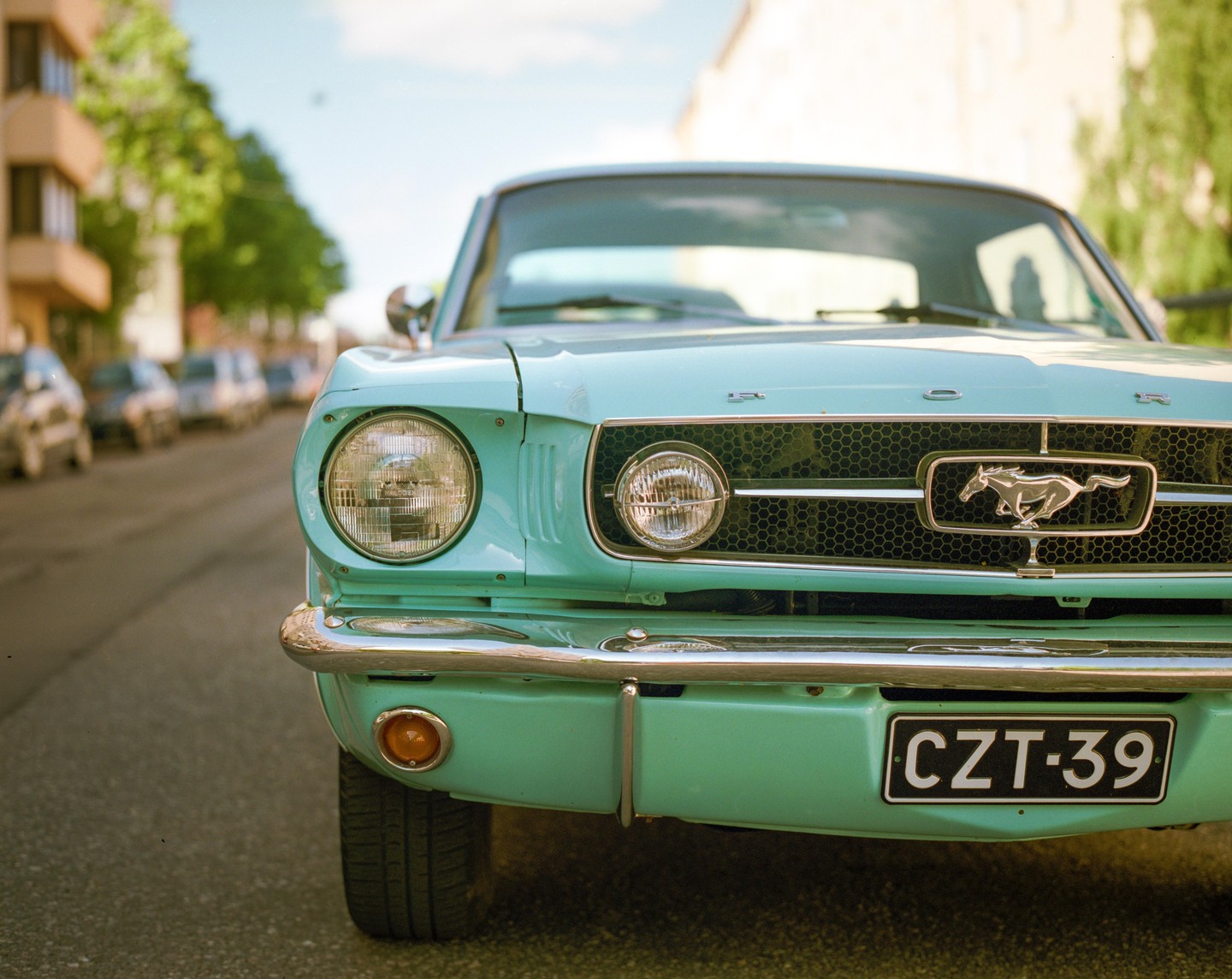 A turquoise vintage car is parked on a street with other cars and buildings in the background.