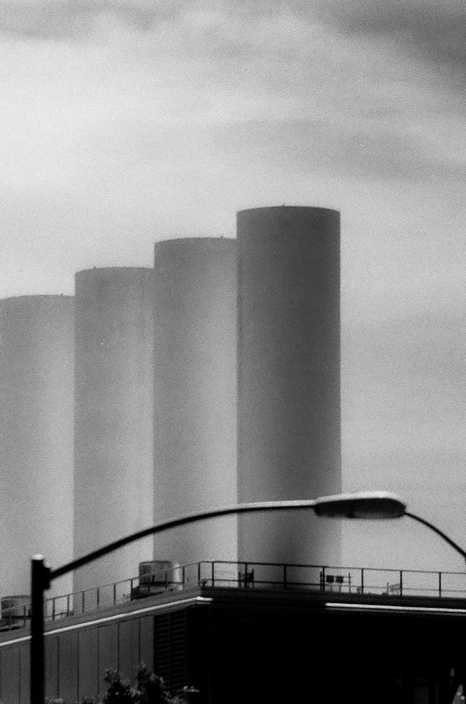Four tall, cylindrical stacks rise behind a building with a street light in the foreground.