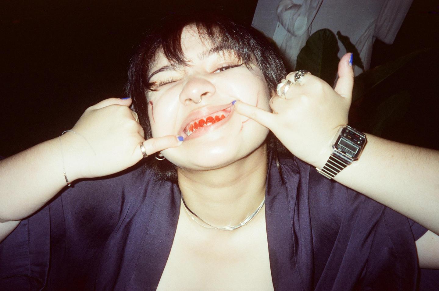 A woman with red candy on her teeth pulls at the corners of her mouth with her fingers.