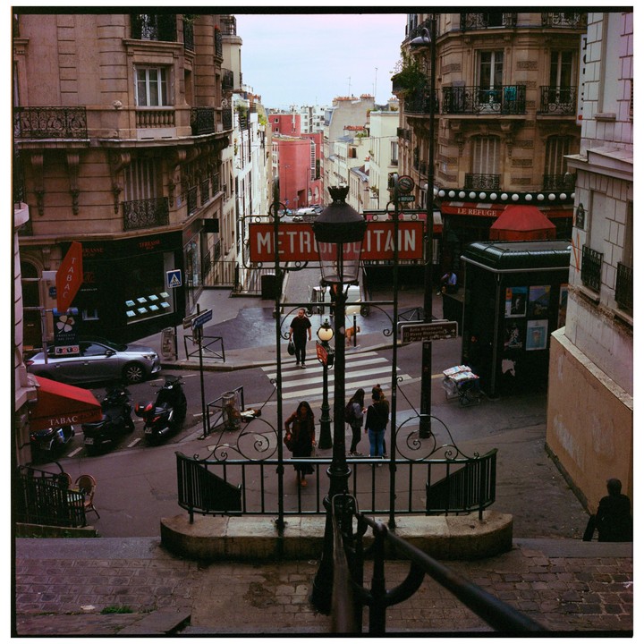 A street in Paris is seen from above, with a metro entrance and several people walking.