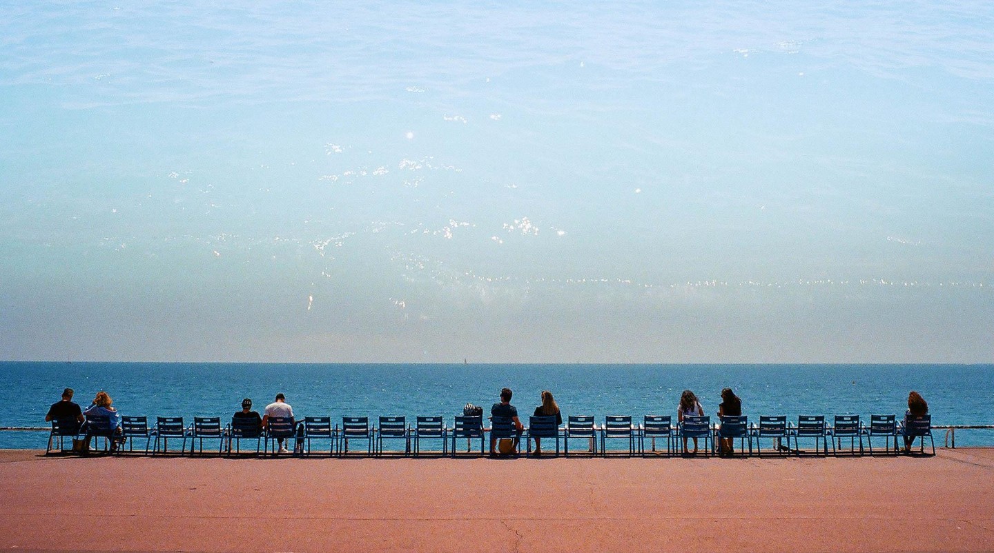 People sit on chairs facing the sea under a hazy sky.