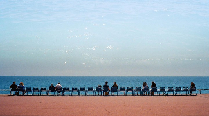 People sit on chairs facing the sea under a hazy sky.
