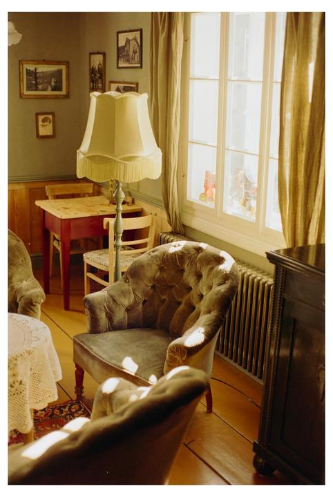 Sunlight streams through a window into a cozy room with vintage furniture and framed pictures on the wall.