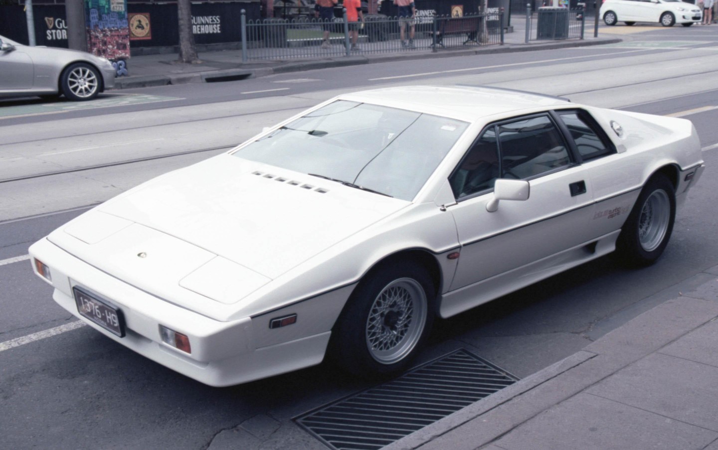 A white Lotus Esprit is parked on the side of a street next to a sidewalk.
