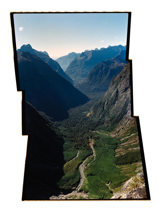 A deep valley with a river and forest is surrounded by mountains under a clear sky.