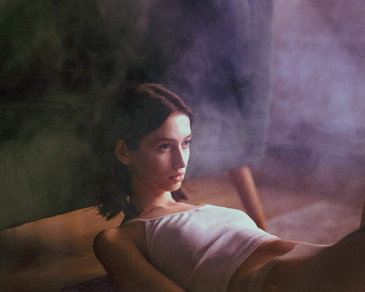 A woman in a white tank top is lying down with smoke around her.