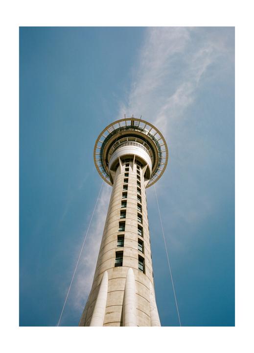 A tall concrete tower with a circular observation deck at the top stands against a blue sky with wispy clouds.