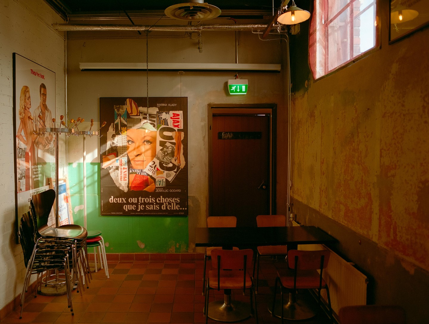 Sunlight streams into a room with a tiled floor, a table with chairs, and movie posters on the wall.
