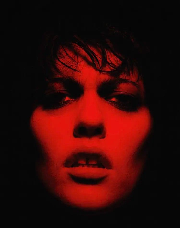 A woman's face is illuminated in red light against a dark background.