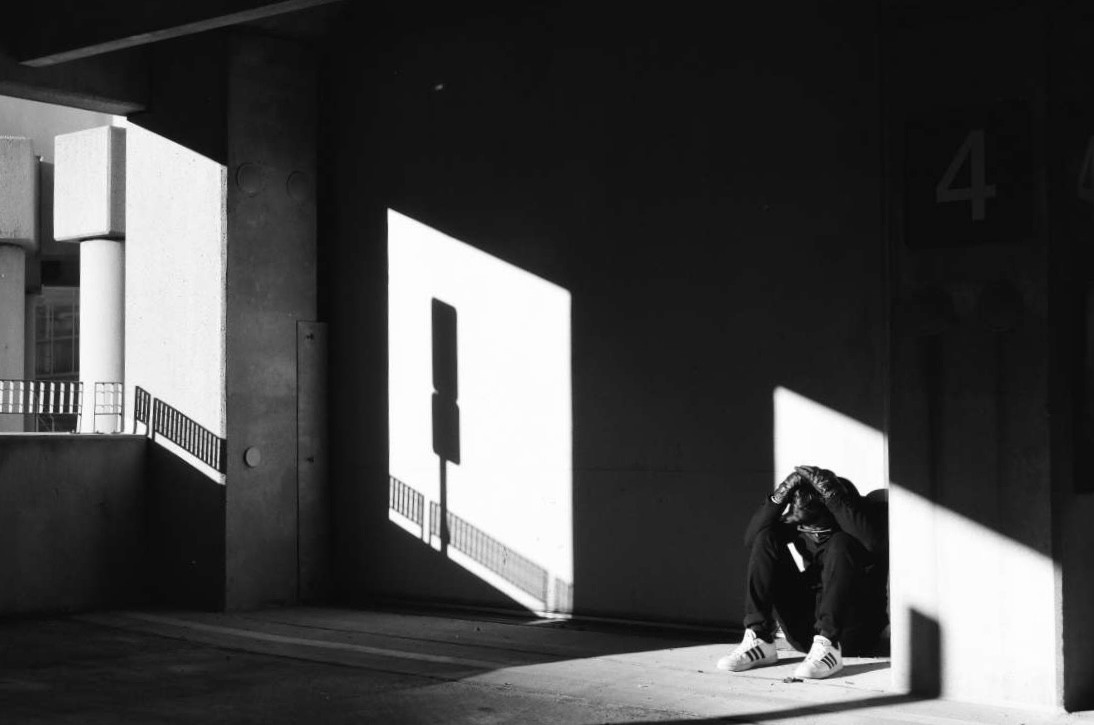 A person sits on the ground in a dark, angular space with strong shadows and highlights.