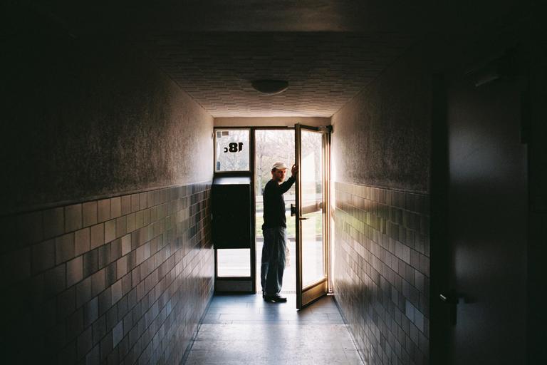 A man stands in a doorway at the end of a long, tiled hallway.