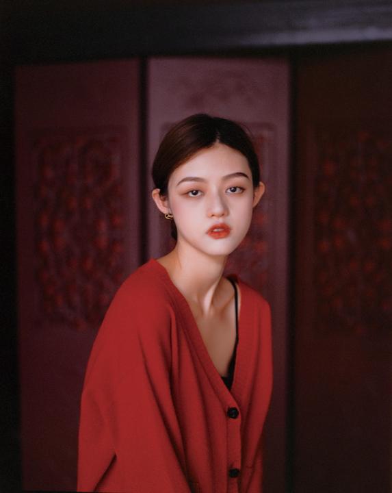 A woman wearing a red cardigan and black top looks directly at the viewer.