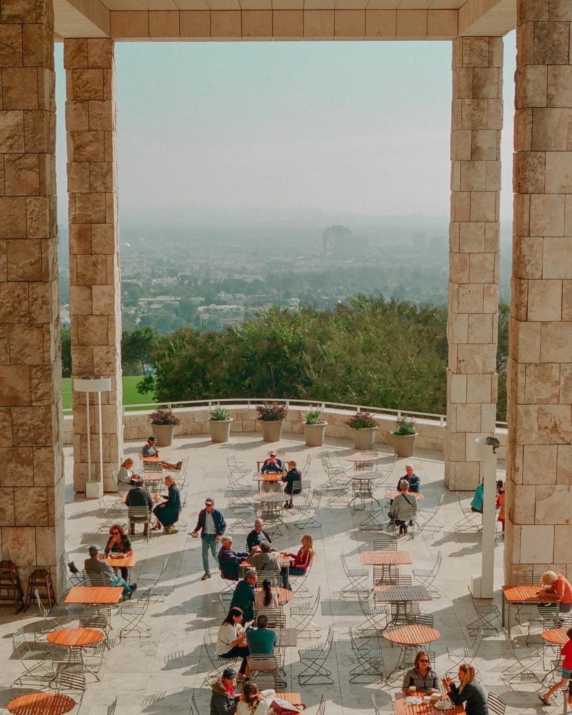 People sit at tables on a patio overlooking a hazy city.