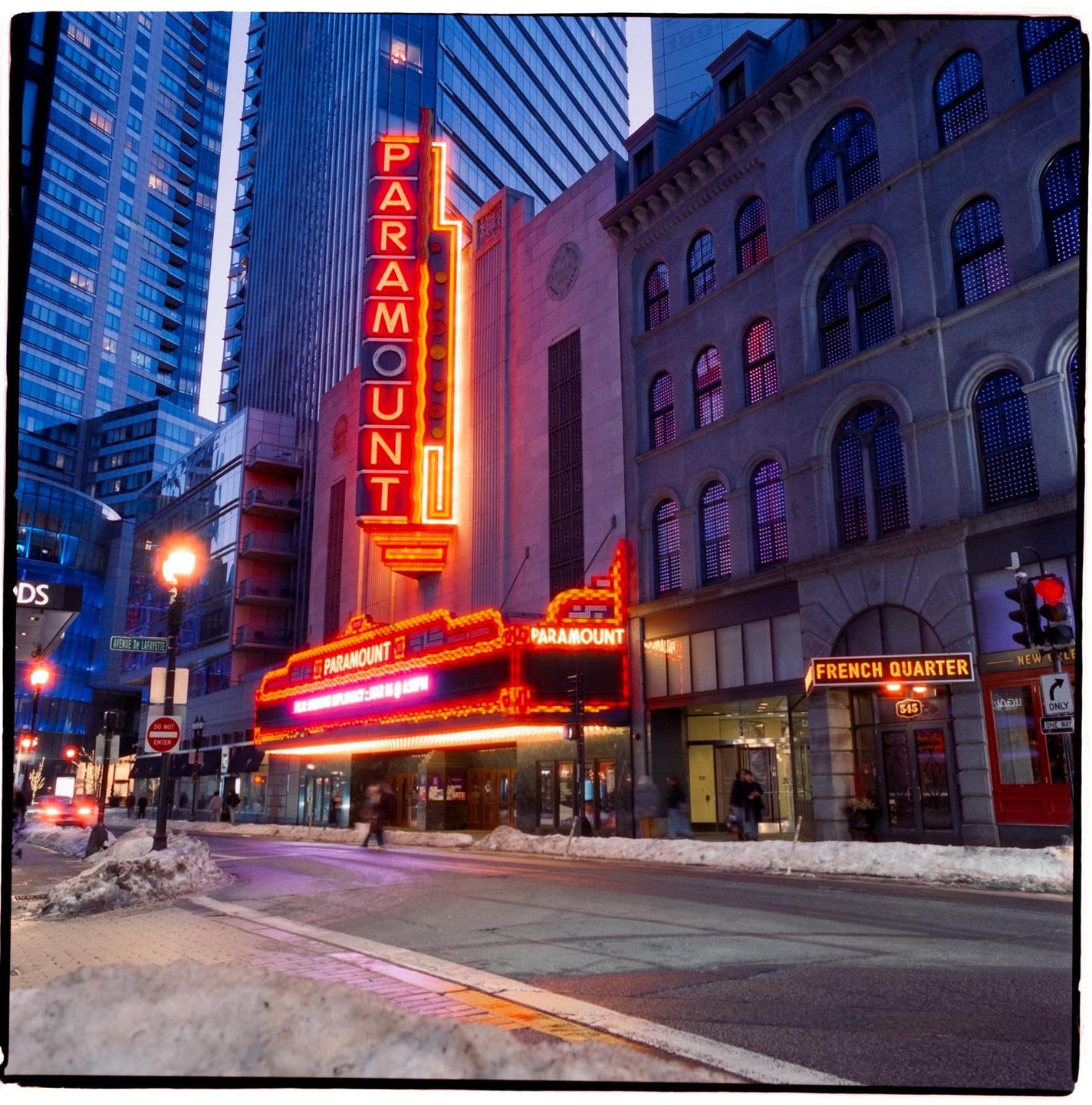 A street scene at dusk shows the Paramount Theatre with its neon sign illuminated, and snow on the ground.