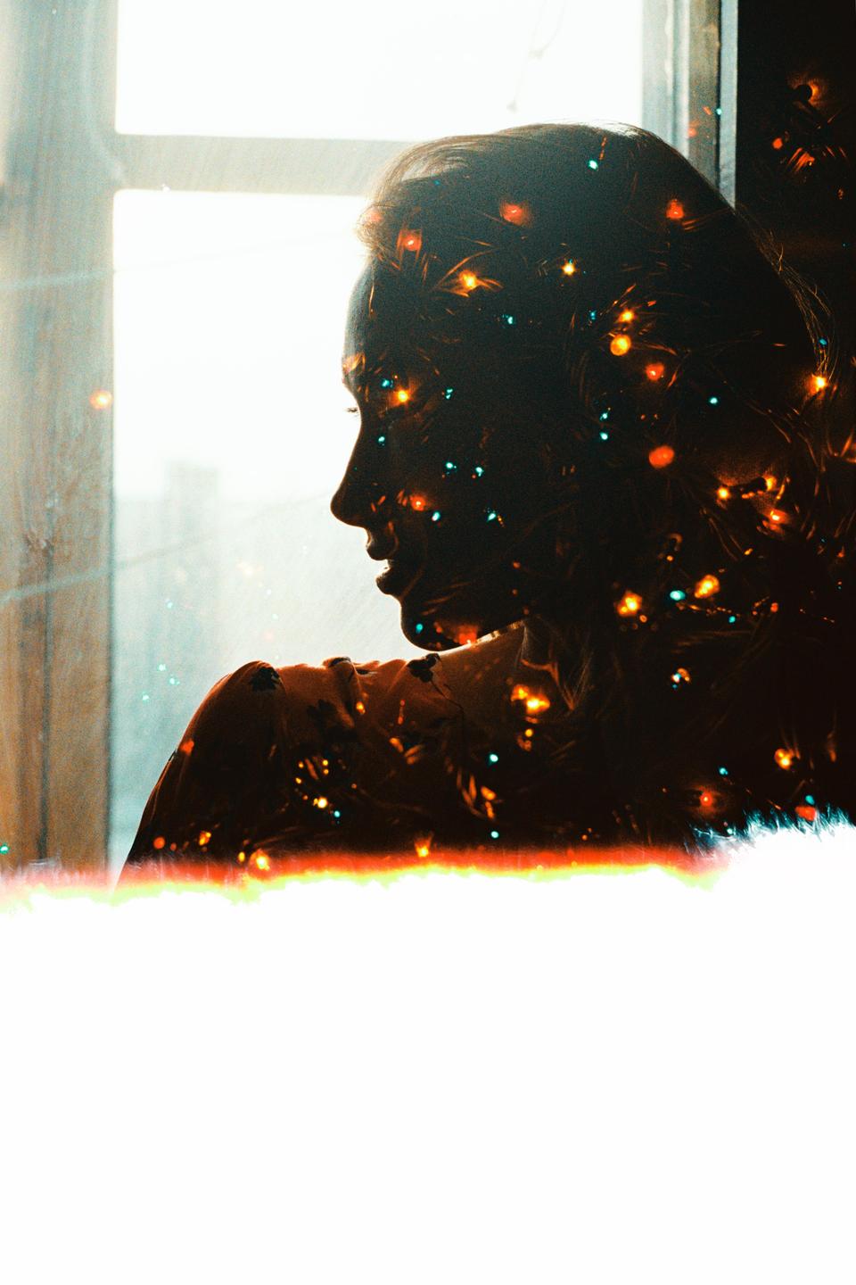 A woman's silhouette is visible in profile, filled with colorful bokeh lights, against a bright window.