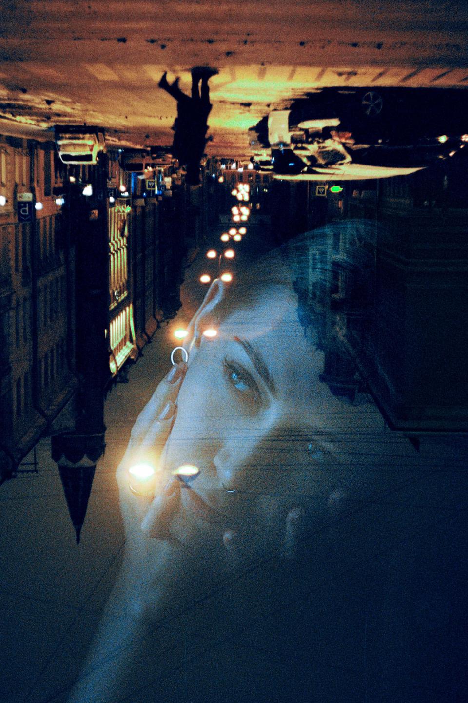A woman's face is superimposed over an upside-down street scene at night.