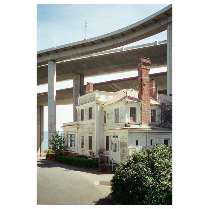 A white house with brick chimneys stands beneath a large concrete overpass.