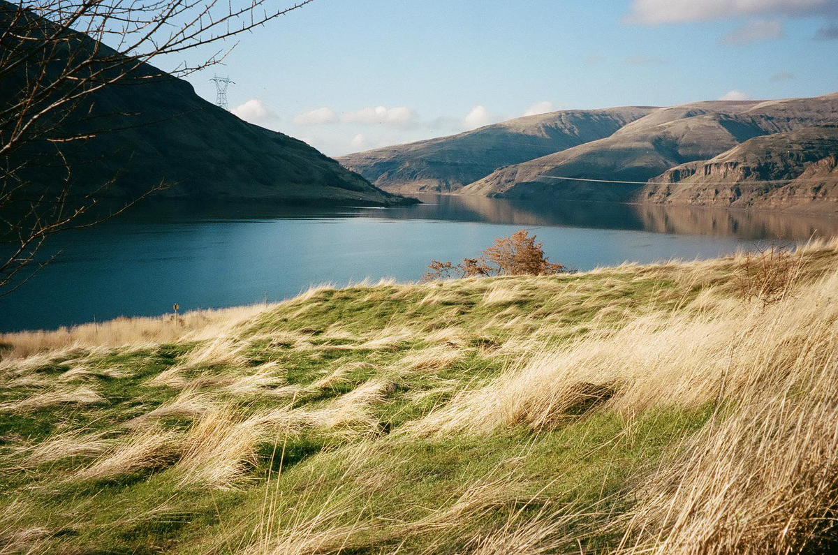 A body of water is surrounded by hills with a grassy slope in the foreground.