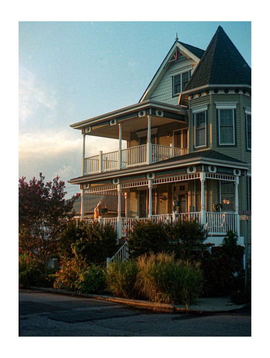 A large house with multiple porches and a turret is illuminated by the setting sun.