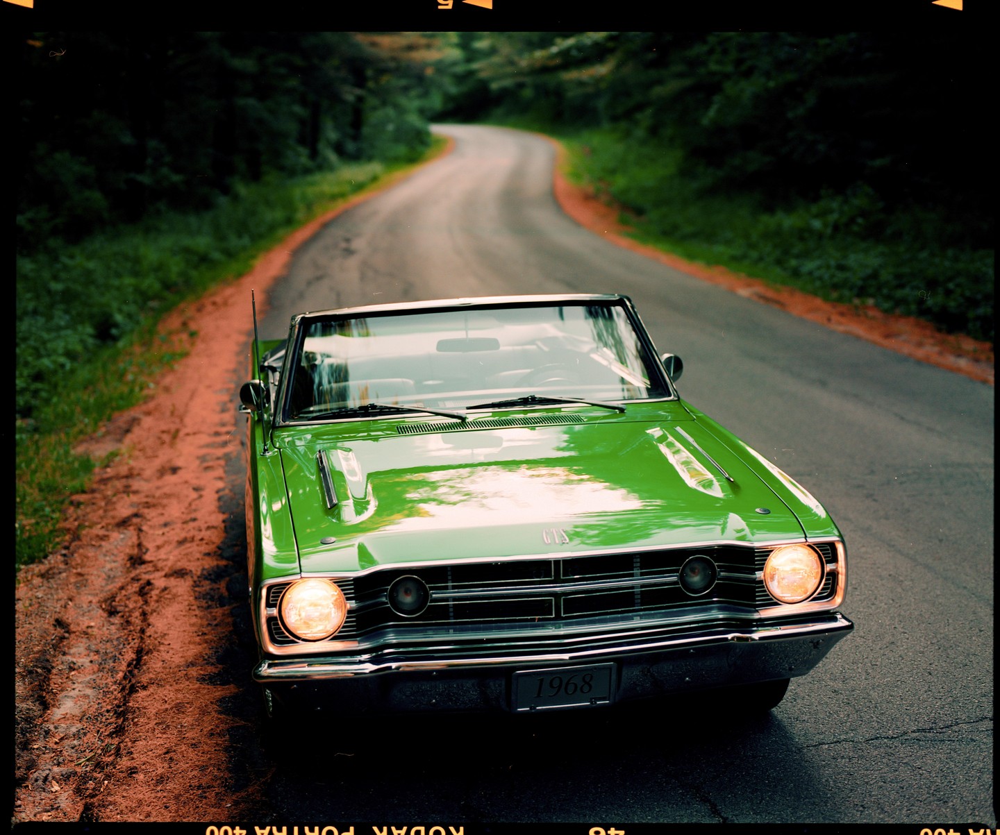 A bright green convertible car is parked on the side of a winding road through a forest.